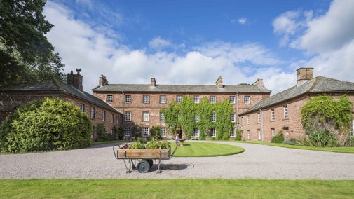 View of the front of the house with a garden trolley and children playing domino at Acorn Bank, Cumbria